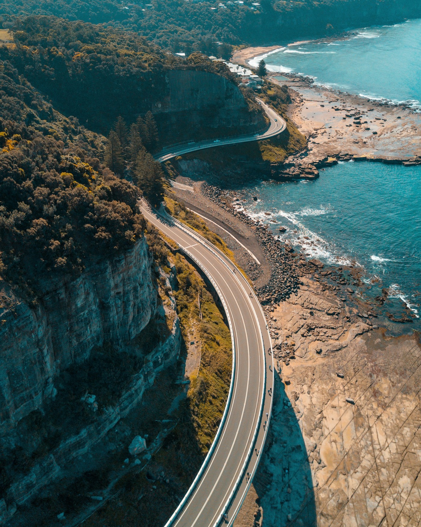 Winding coastal road beside cliffs and blue ocean, used as travel inspiration